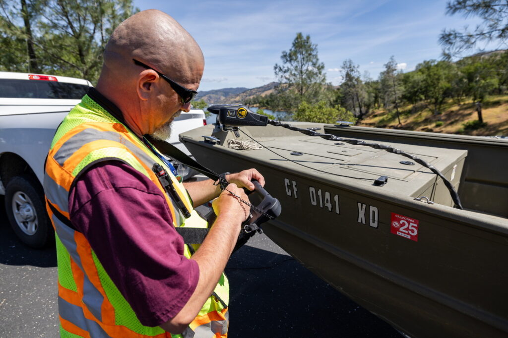 A person in a high-visibility vest operates a device attached to a boat marked with California registration.