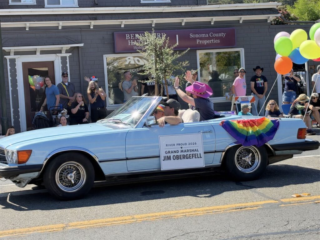 Jim Obergefell in a pink cowboy hat waves from a light blue convertible on Main Street in Guerneville. Photo: Roger Coryell/Bay City News